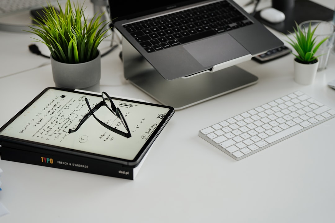 a desk with a laptop, keyboard, glasses and a potted plant